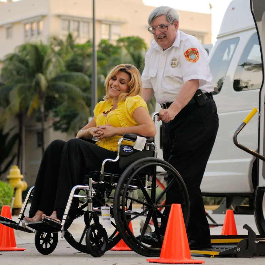 A woman in a wheelchair is being helped onto a vehicle with a lift service.