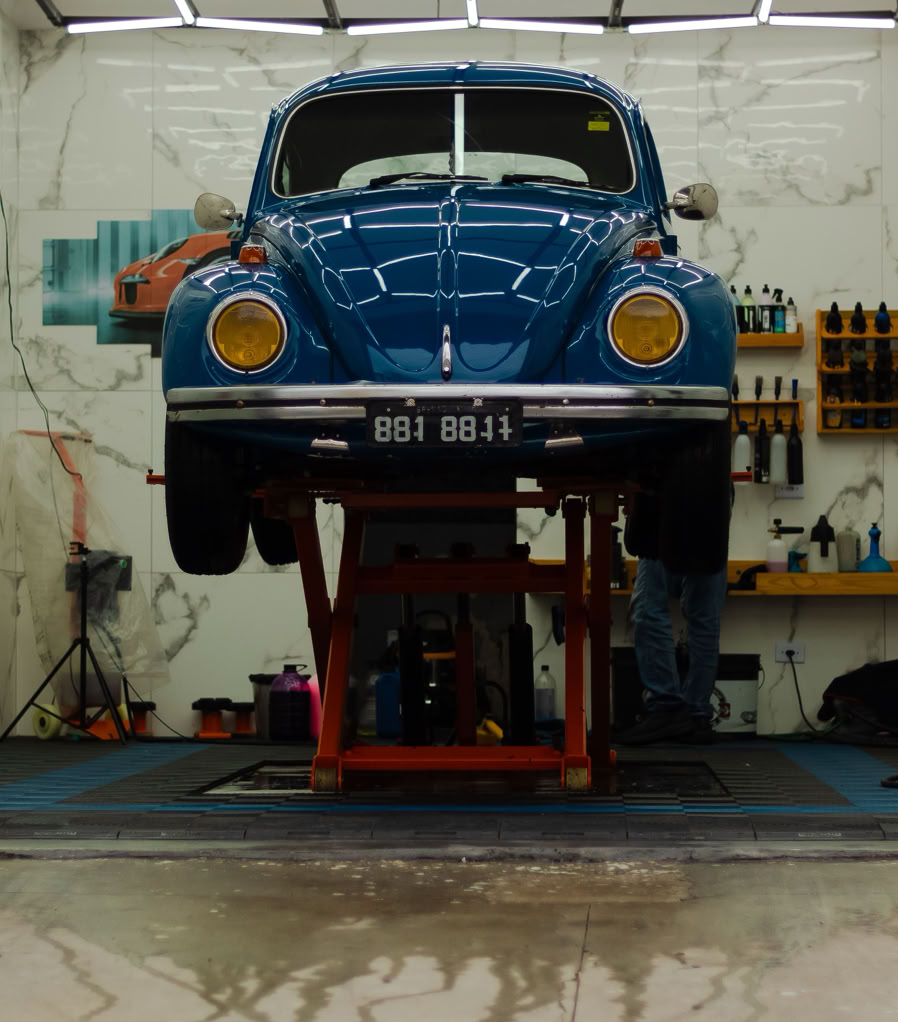 A classic blue Volkswagen Beetle being serviced in a modern auto repair garage.