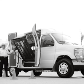 A white van equipped with a wheelchair lift is being inspected outdoors by an adult male.