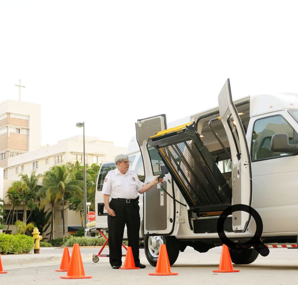 A security guard operates a wheelchair lift on a van outside a medical facility.