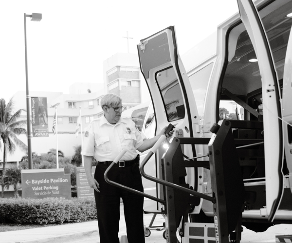 A person demonstrating the use of a van lift for accessibility in an outdoor setting.