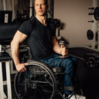 Strong man in a wheelchair holding a dumbbell, showcasing determination and fitness at the gym.