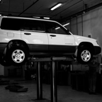 Black and white photo of a Subaru SUV lifted in an auto repair shop.