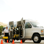 A driver standing by a wheelchair accessible van with open doors and a ramp, surrounded by cones.