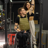 A man in a wheelchair receives supportive guidance from a fitness trainer at the gym.